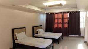 A room with two single beds, a large window with curtains, and a ceiling light fixture. - ValueNest Stay (Naga)