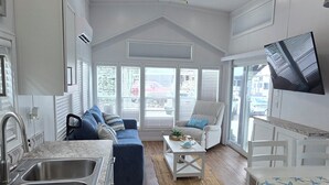 A spacious living area with a kitchen, a ceiling fan, and a large window. - Happier in the keys- waterfront tiny home in Key Largo (Key Largo)