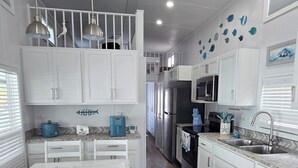 A modern kitchen with white cabinets, a wooden floor, and a dining area with white chairs. - Happier in the keys- waterfront tiny home in Key Largo (Key Largo)