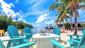 A beachside seating area with turquoise chairs and a white table, overlooking the sea with boats and palm trees in the background. - Happier in the keys- waterfront tiny home in Key Largo (Key Largo)