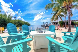 Un espace aménagé avec des chaises Adirondack turquoise et une table blanche, situé au bord de la plage et offrant une vue sur la mer.