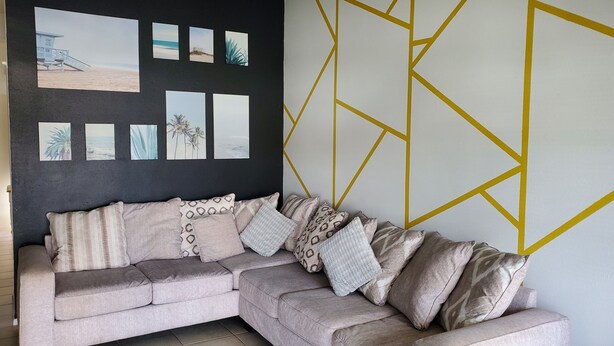 A beige sectional sofa with patterned cushions, a dark wall with beach-themed artwork, and a geometric gold accent wall. - A bit of Tampa sunshine  (Tampa)