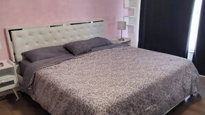 A bedroom with a bed, a nightstand, a wall-mounted shelf, and a window with curtains. - A bit of Tampa sunshine  (Tampa)