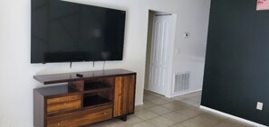 Una habitación con una televisión de pantalla plana montada en la pared, un mueble de madera con cajones, una puerta blanca y un respiradero en la pared.