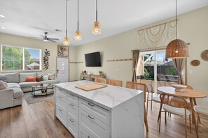 A modern kitchen with a marble island, wooden dining set, and a flat-screen TV. - Elegant Mediterranean 3BR Haven Citrus Heights (Citrus Heights)