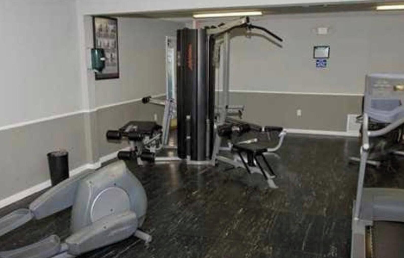 Ein Fitnessraum mit Trainingsgeräten, einem an der Wand befestigten Fernseher und einem Mülleimer.