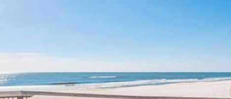 Une vue sur la plage avec une terrasse en bois et un ciel dégagé.