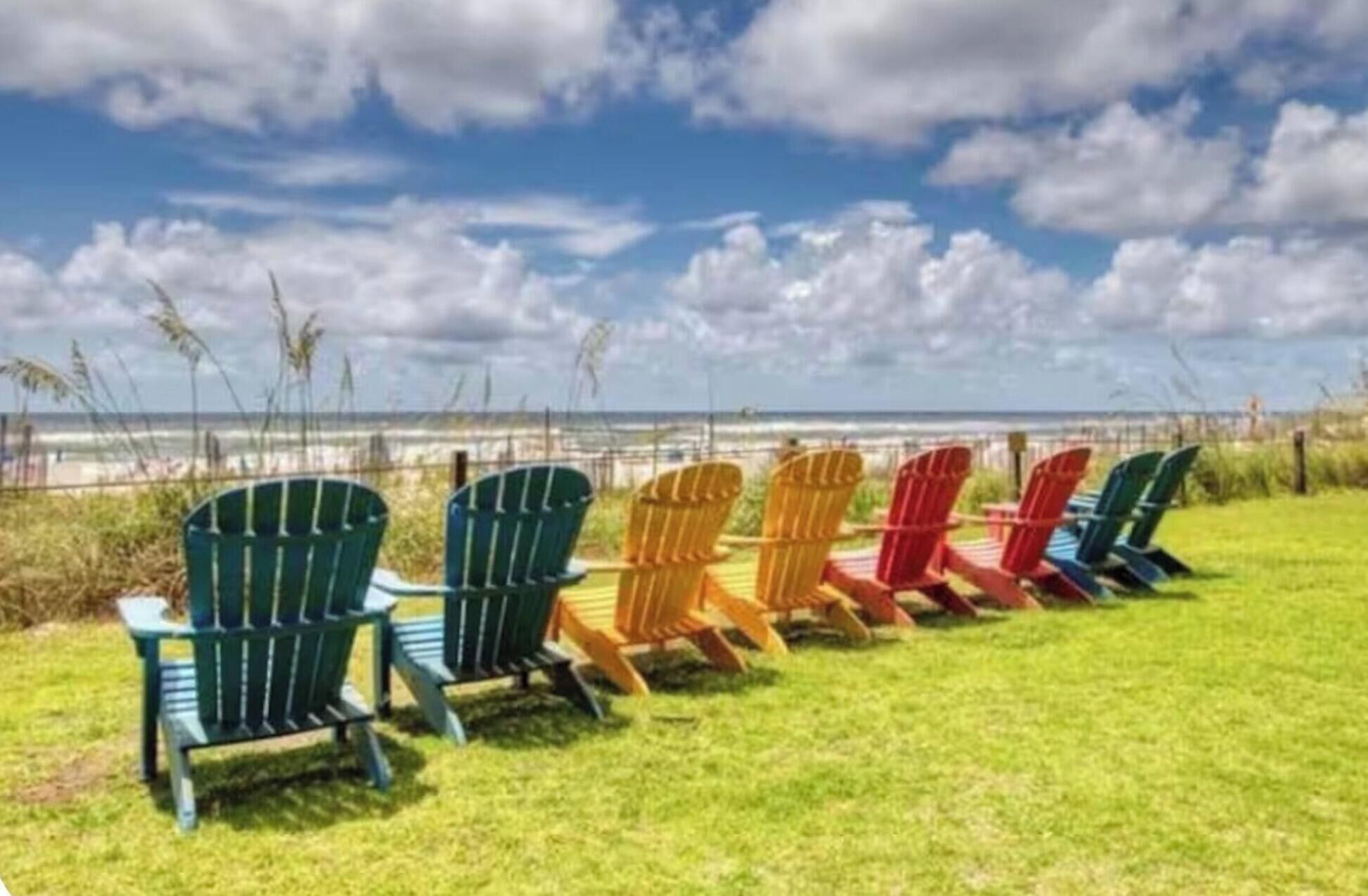 Une rangée de fauteuils Adirondack est disposée sur une pelouse, offrant une vue sur l’océan.