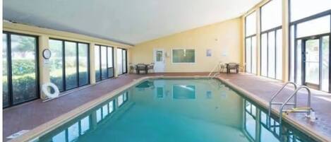 An indoor swimming pool with clear glass walls, a tiled floor, and a lifeguard chair.