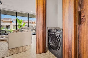 A modern living room with a sofa, a washing machine, and a view of a residential area. - Quiet 2BR Penthouse w Private Pool | Gym | CoWork (Tulum)
