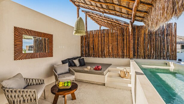 Zona junto a la piscina con un sofá, sillas, una mesita con fruta y un colgador de luz.