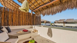 Una terraza en la azotea con techo de paja, mobiliario de mimbre y una cesta de frutas.