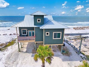 A two-story beach house with a balcony, a small deck, and a view of the ocean.