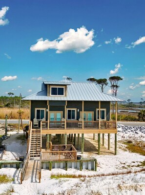 A two-story house with a balcony, wooden deck, and a view of the beach.