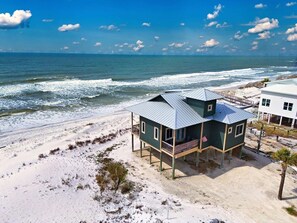 A beachfront house with a balcony, a view of the ocean, and a sandy beach.