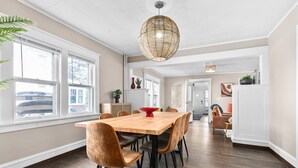 A spacious dining area with a wooden table and chairs, large windows, and a hanging light fixture. - Roomy Central Hub • Games, Fire Pit & Downtown Fun (Oshkosh)