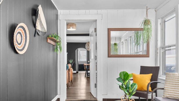 A hallway with a dark wall, a mirror, a wicker chair, a sofa, and a plant. - Roomy Central Hub • Games, Fire Pit & Downtown Fun (Oshkosh)
