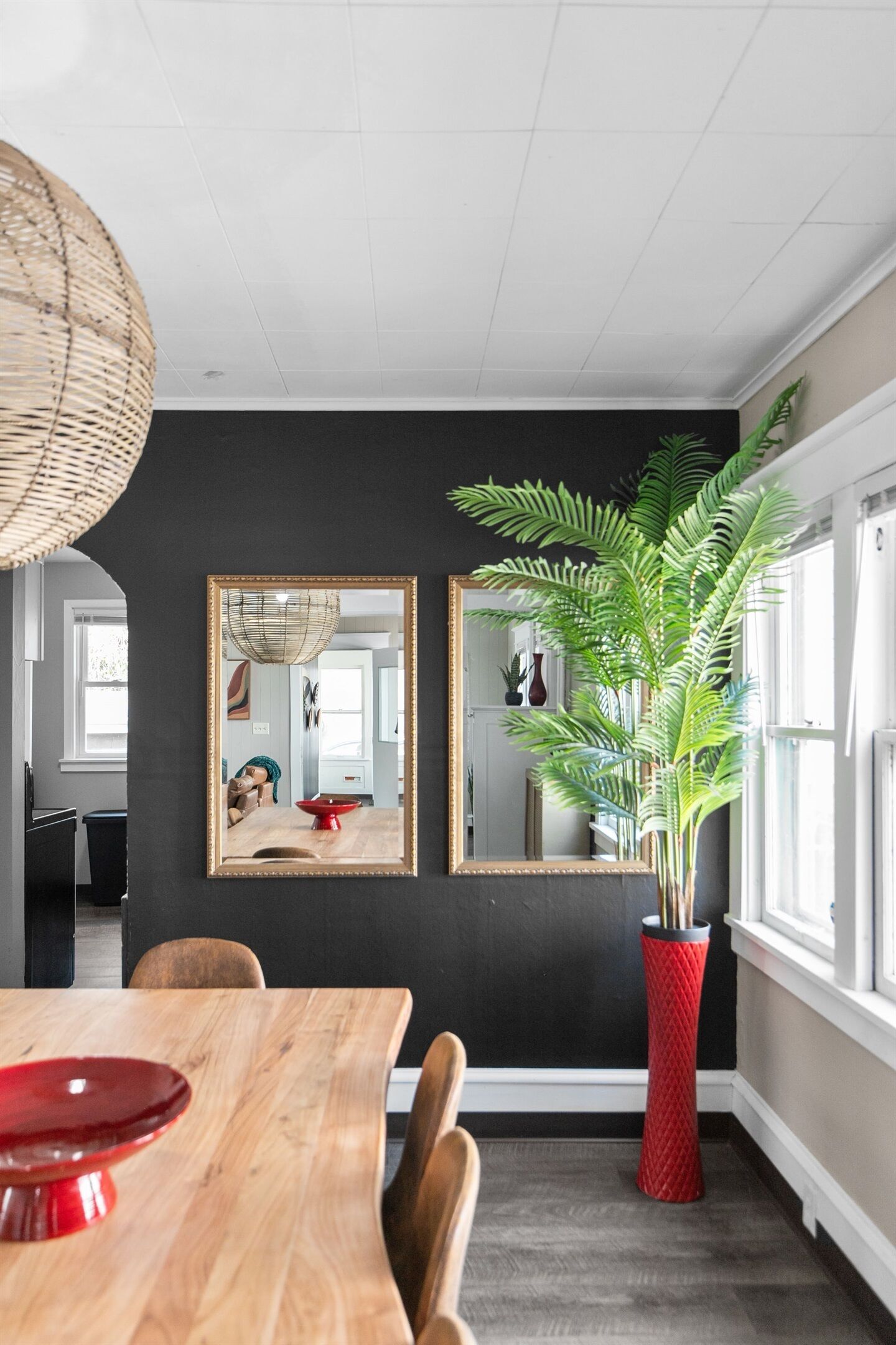 Un coin repas avec une table en bois, des chaises, un vase rouge et un grand miroir au mur.