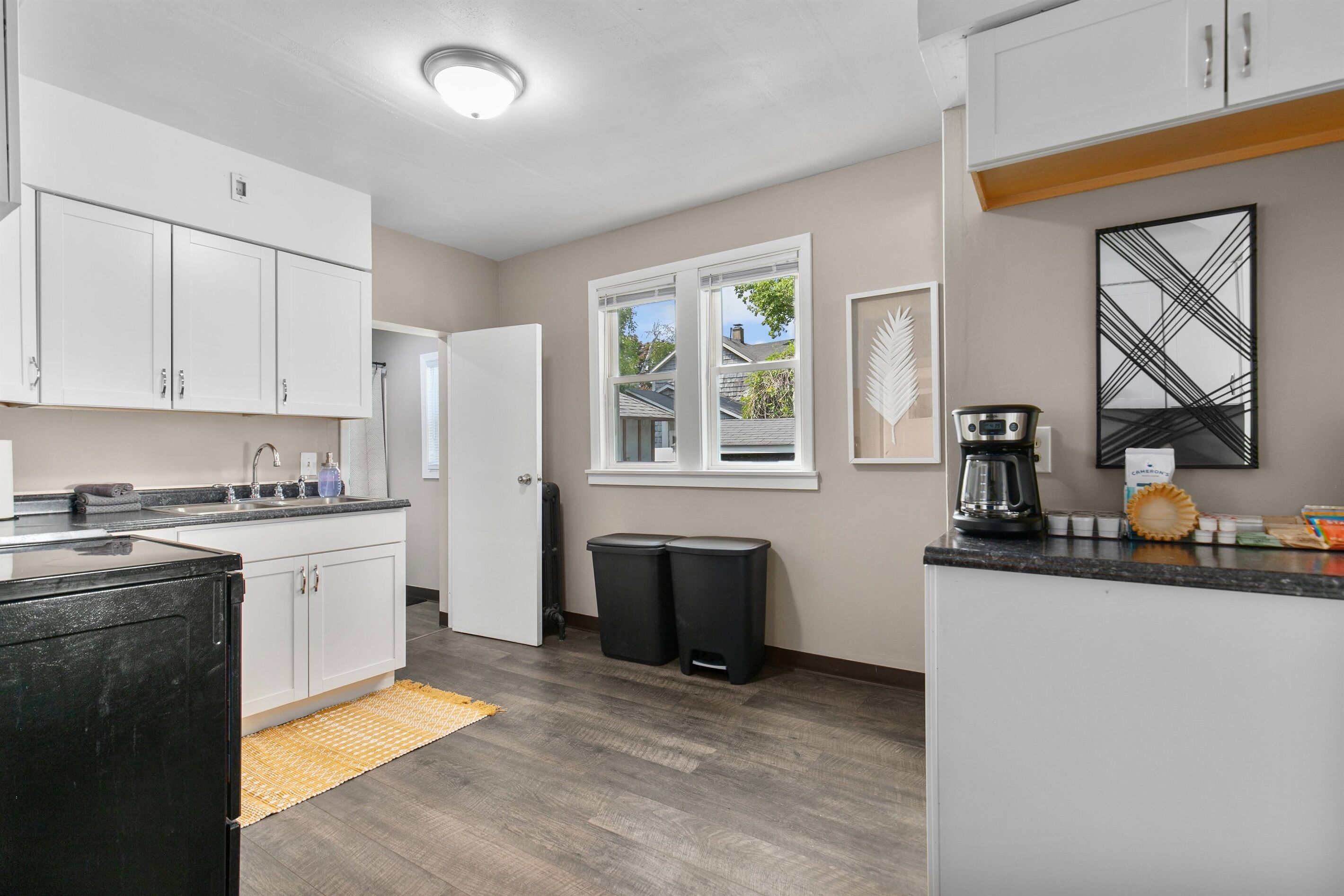 A modern kitchen with white cabinets, a black refrigerator, a coffee maker, and a window with a view of the outside.