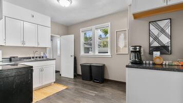A modern kitchen with white cabinets, a black refrigerator, a coffee maker, and a window with a view of the outside.