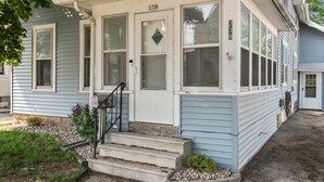 A two-story house with a front porch, numbered 238, featuring a set of concrete steps leading to the door. - Roomy Central Hub • Games, Fire Pit & Downtown Fun (Oshkosh)