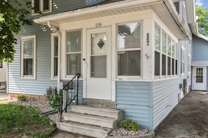 Une maison à deux étages avec un porche à l’avant, portant le numéro 238, et dont l’entrée est accessible par un escalier en béton.