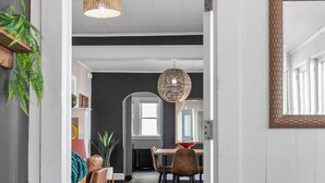 A hallway leading to a dining area with a wooden floor, a hanging light fixture, and a mirror on the wall. - Roomy Central Hub • Games, Fire Pit & Downtown Fun (Oshkosh)