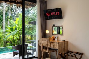 Habitación con escritorio, silla, televisor y vistas a una piscina y follaje.