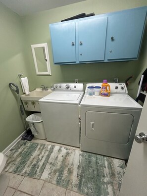 A laundry area with two washing machines, a dryer, a trash can, and a cabinet above the machines. - Sunsets! Beachfront!  Gulf view! 2-bedroom condo in beautiful Perdido Key, FL (Pensacola)