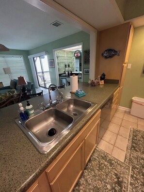A kitchen with a double sink, wooden cabinets, a fish decoration, and a dining area with a table and chairs. - Beachfront Sunset Haven w/ Big Balcony, Gulf View in Beautiful Perdido Key, FL (Pensacola)