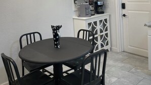 A dining area with a round table, black chairs, a decorative vase, a ceiling light fixture, a microwave, a coffee maker, and a white cabinet.