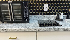 A kitchen with a black microwave, a white blender, and various pots and pans on shelves.