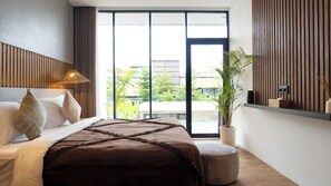 A modern hotel room with a large bed, a potted plant, and a view of greenery outside. - Aquamarine Villa 8A (Canggu)