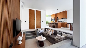 Ein modernes Wohnzimmer mit Fernseher, Sofa, Couchtisch und einer Küchenzeile mit Holzausbau und einer Bar.