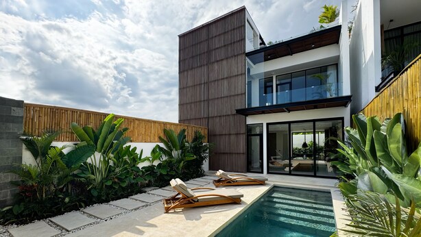 Ein modernes Haus mit Swimmingpool, Liegestühlen und üppiger Bepflanzung.