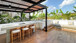 Eine Dachterrasse mit Holzboden, einer Sitzecke mit Kissen und Blick auf üppige tropische Pflanzen.