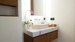 A bathroom with a white sink, a mirror, a plant, and wooden cabinets. - Aquamarine Villa 8A (Canggu)