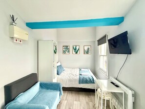 A bedroom with two beds, a desk, a TV, and a window. - London Camden studio sleeps 3 (London)