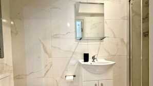 A bathroom with a toilet, a sink with a mirror above it, and a shower area. - London Camden studio sleeps 3 (London)