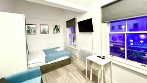A bedroom with a bed, a desk, a TV, and a window with a view of the city. - London Camden studio sleeps 3 (London)