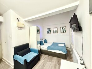A compact room with a sofa, a bed, a wardrobe, and a TV mounted on the wall. - London Camden studio sleeps 3 (London)