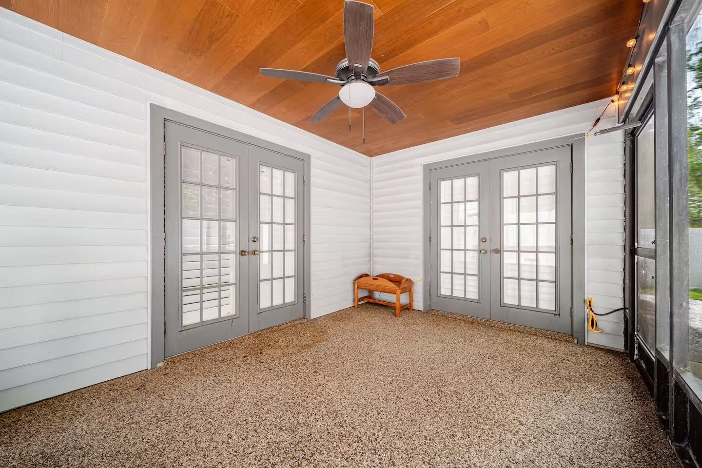 A room with two grey doors, a ceiling fan, and a bench.