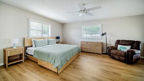A bedroom with a bed, bedside tables, a dresser, a chair, a ceiling fan, and windows.