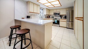 A modern kitchen with a central island, bar stools, stainless steel appliances, and a skylight.