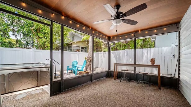 A covered outdoor patio with a ceiling fan, a barbecue grill, and a table with stools.