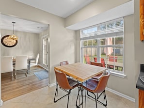A dining area with a wooden table and chairs, a clock on the wall, and a large window with a view of the outdoors. - Fully Fenced Backyard - 5BR with Kings - Cooler Pooler - Pets Welcome! (Pooler)