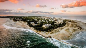 Vue aérienne d’une zone résidentielle côtière, avec des maisons, une plage et une jetée.