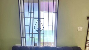 A dark brown sofa with patterned cushions, a window with metal bars, and a patterned floor.