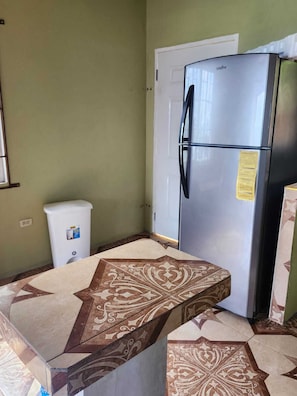 A kitchen with a stainless steel refrigerator, a white trash bin, and patterned floor tiles.