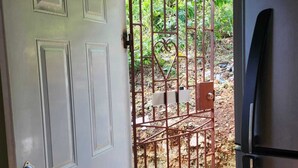 An open door leading to a garden with a metal gate, a refrigerator, and a tiled floor.